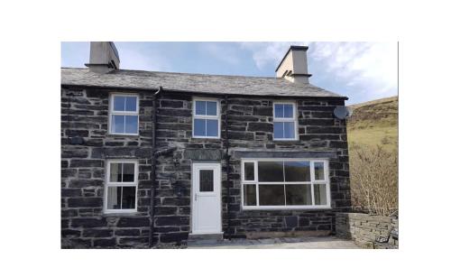a stone house with a white door and windows at Yr Hen Siop - 4 bed welsh cottage in Snowdonia in Penmachno