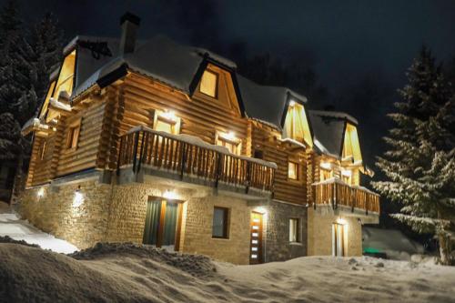 una casa di tronchi con luci accese nella neve di Drvena Kuca RUŽA a Kopaonik