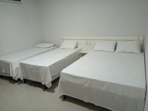 two beds in a room with white walls at Topazzo Hotel in Uruara