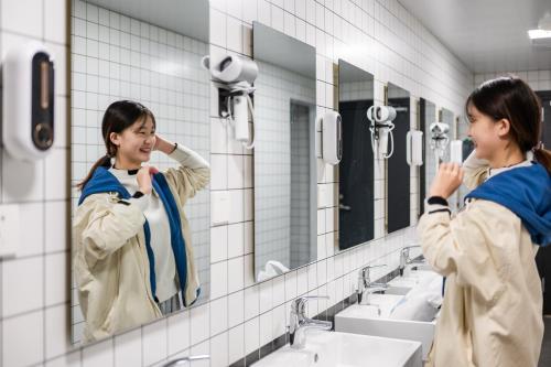 a woman looking at herself in a bathroom mirror at Dayin Youth Hostel - East Nanjing Road & People's Square & The Bund -Large Social Area -Bar -Café -Gym -Free Laundry Luggage Storage -24H Front Desk -English Service in Shanghai