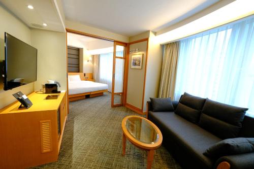 a hotel room with a couch and a tv and a bed at South Pacific Hotel in Hong Kong