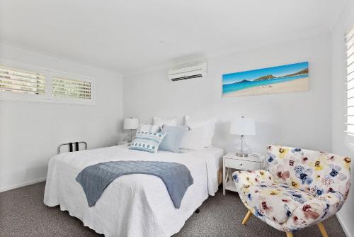 a white bedroom with a bed and a chair at HideAway on Tallean in Nelson Bay