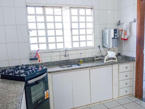 a kitchen with a stove and a sink and a window at Casa Azul Antares 3 Quartos - Pet Friendly in Londrina