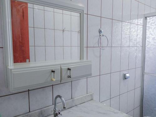 a white tiled bathroom with a sink and a mirror at Casa Azul Antares 3 Quartos - Pet Friendly in Londrina