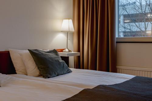a bedroom with a bed with a lamp and a window at First Hotel Jörgen Kock in Malmö