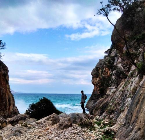 un hombre parado en las rocas cerca del océano en Casa belvedere Sa Costa, en Dorgali