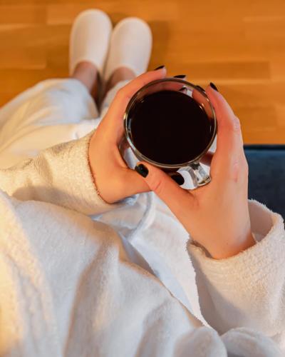 a woman laying on a bed holding a cup of coffee at First Hotel Jörgen Kock in Malmö