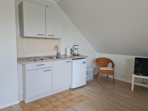 uma cozinha com armários brancos, um lavatório e uma cadeira em "Pappelhof - Whg 10" em Grömitz