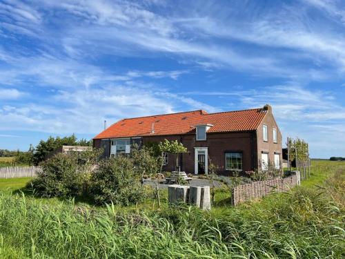 a brick house with a red roof in a field at B&B Bouwmanshoeve in Burgh Haamstede