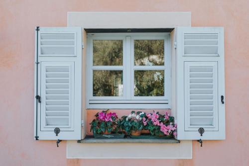 a window with white shutters and flowers on a pink wall at Casa Aquarela in Cogorno