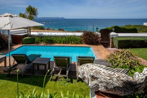 a swimming pool with chairs and an umbrella and the ocean at La Fontaine Guest House Hermanus in Hermanus
