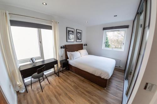 a bedroom with a bed and a desk and two windows at Oakhill Apartment in Aberdeen