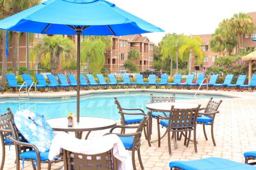 a pool with tables and chairs and a blue umbrella at Hilton Vacation Club Polynesian Isles Kissimmee in Kissimmee