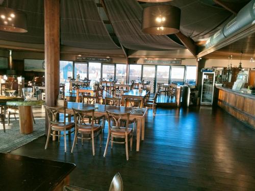 een restaurant met houten tafels, stoelen en ramen bij BJ Chalets - De Rug 1 - Vakantiepark Lauwersoog - LUXE, kindvriendelijke chalet MET vaatwasser! Vroege incheck! in Lauwersoog