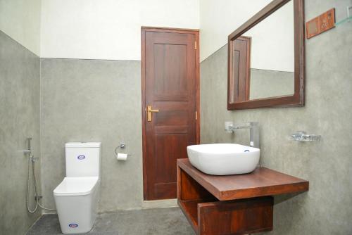 a bathroom with a sink and a toilet and a mirror at Yehen's Villa in Unawatuna