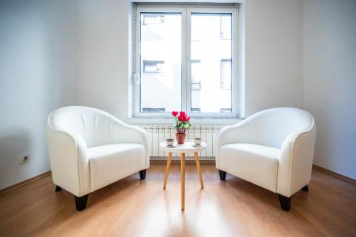 two white chairs and a table with a vase of flowers at Bright and Modern 1BDR Apartment in the Center in Sarajevo