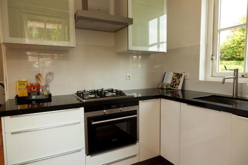 een keuken met witte kasten en een fornuis met oven bij Het Eerste Huisje vacation home in Noordwijk aan Zee