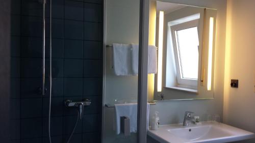 uma casa de banho com um lavatório e um chuveiro com um espelho. em Hotel Henry em Dreieich