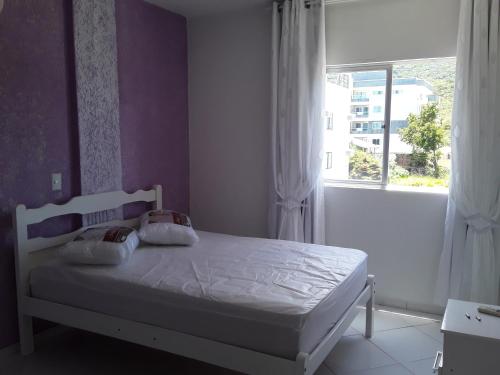 1 dormitorio con cama blanca y ventana en Apartamento de temporada, en Bombinhas
