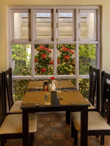 a table with chairs and a window with flowers at Rosewood by Nature Resorts and Stays in Ooty