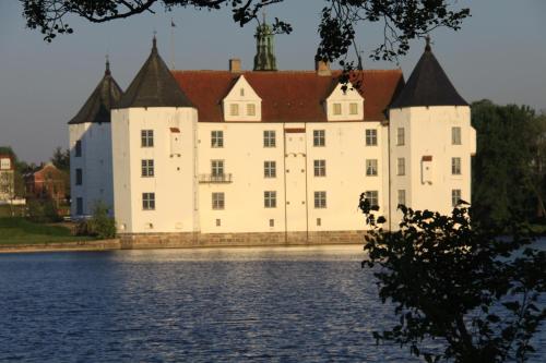 un gran castillo blanco con techo rojo sobre el agua en Ferienwohnung Landhaus, en Maasbüll