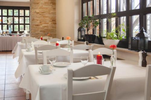 a restaurant with white tables and white chairs and windows at Hotel Omega in Moers