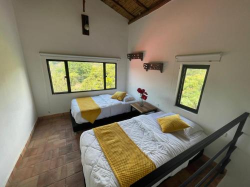 a bedroom with two beds and two windows at Hotel Casas de Campo El Ciruelo in San Gil