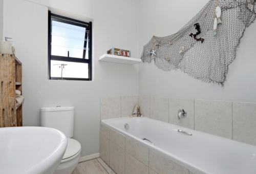 a bathroom with a tub and a toilet and a window at Cheerful Cottage on Britannia Beach, West Coast in Britannia Bay