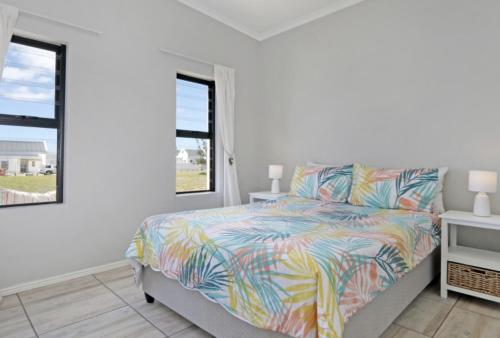 a bedroom with a bed and two windows at Cheerful Cottage on Britannia Beach, West Coast in Britannia Bay