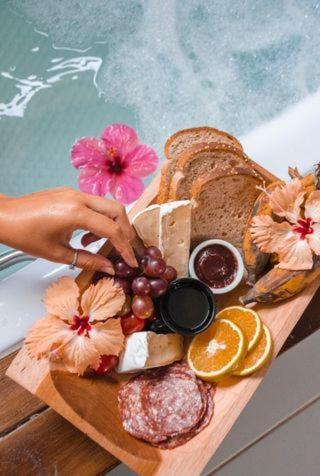 a tray of food with bread and fruit on a cutting board at Sapê Guest Hotel in Praia do Rosa