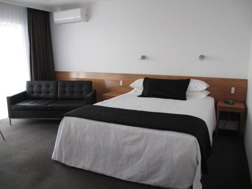 a bedroom with a large bed and a black chair at Auto Lodge in New Plymouth
