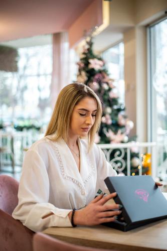 a woman sitting at a table with a laptop at Garni Hotel Lotos in Niš