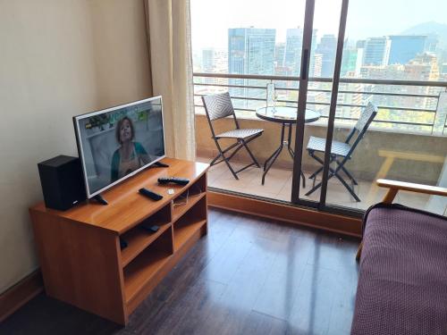 een woonkamer met een televisie en een balkon met een tafel bij Departamentos Pontoni Escuela Militar in Santiago