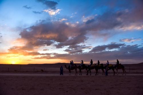 a group of people riding camels in the desert at sunset at Agafay Pearl Camp Marrakech in Marrakech