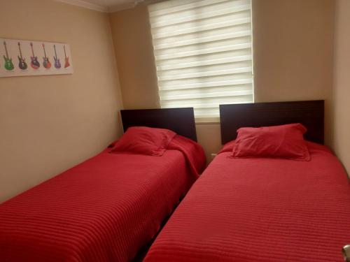 Cette chambre dispose de 2 lits avec des draps rouges et d'une fenêtre. dans l'établissement Acogedor Departamento en El Tabo, à El Tabo