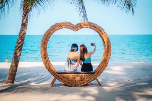 dos chicas sentadas en una silla con forma de corazón en la playa en Khanom Sea Beach Resort, en Nakhon Si Thammarat