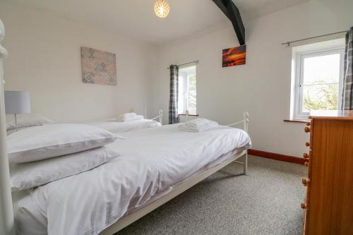 two beds in a white room with two windows at The Stable in Bude