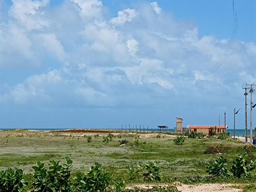 a field of grass with a building and the ocean at Arco Mundial Taíba in Taíba