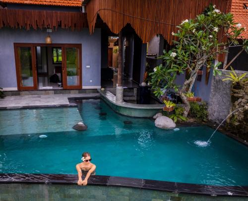 a man sitting in a swimming pool in a house at Uma Jala Villa Ubud in Ubud