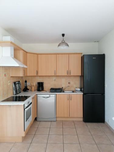une cuisine avec un réfrigérateur noir et des armoires en bois dans l'établissement LES HAUTS VENTS, à Saint-Pol-de-Léon