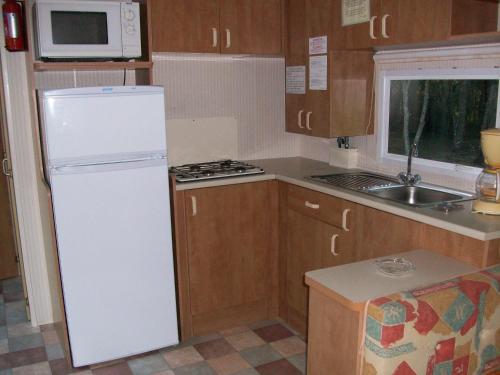 La cuisine est équipée d'un réfrigérateur blanc et d'un four micro-ondes. dans l'établissement Mobilhome 1 calme et tranquilité, à Vendays-Montalivet