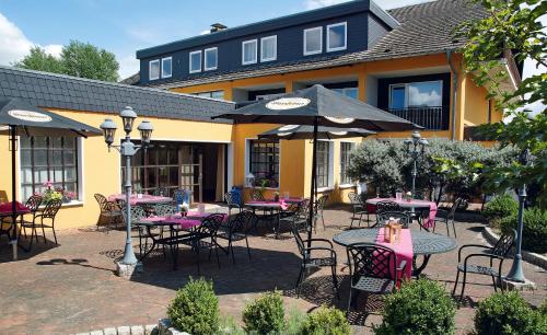 a group of tables and chairs with umbrellas in front of a building at AVALON Hotelpark Königshof in Königslutter am Elm