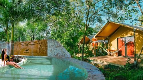 a woman sitting in a swimming pool next to a house at Serenity Authentic Glamping Tulum in Xpu Ha