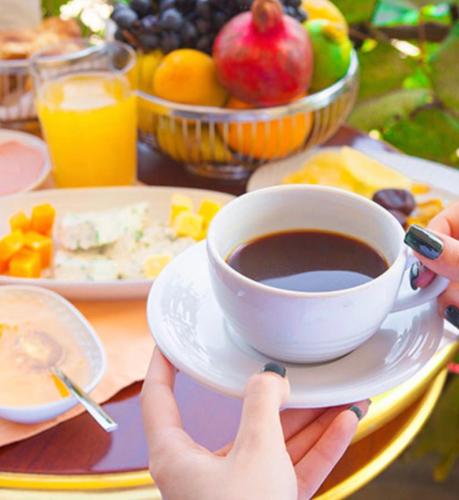 una persona sosteniendo una taza de café en una mesa con fruta en City-Hotel Aschaffenburg, en Aschaffenburg