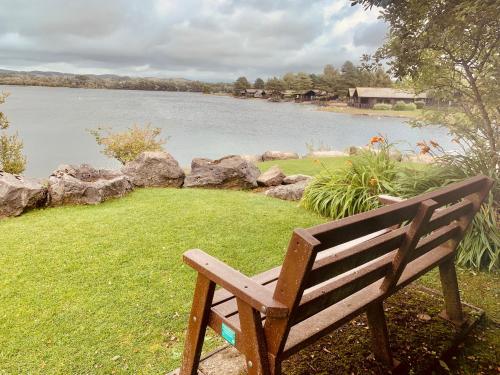 a wooden bench sitting next to a body of water at Keer Side Lodge, Luxury lodge with private hot tub at Pine Lake Resort in Carnforth