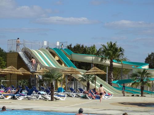 un toboggan aquatique dans un complexe hôtelier avec des gens dans une piscine dans l'établissement Escape MobilHome aux Dunes de Contis, à Saint-Julien-en-Born