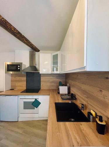La cuisine est équipée de placards blancs et d'un évier noir. dans l'établissement CHEZ FIFI - studio 28m2 - hyper centre - wifi, à Cassis