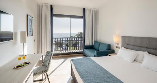 コニル・デ・ラ・フロンテーラにあるIlunion Calas de Conilのベッド、デスク、バルコニーが備わるホテルルームです。