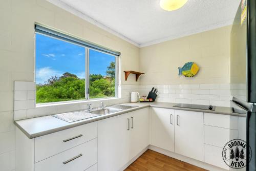 a white kitchen with a sink and a window at Beachside at Brooms in Brooms Head