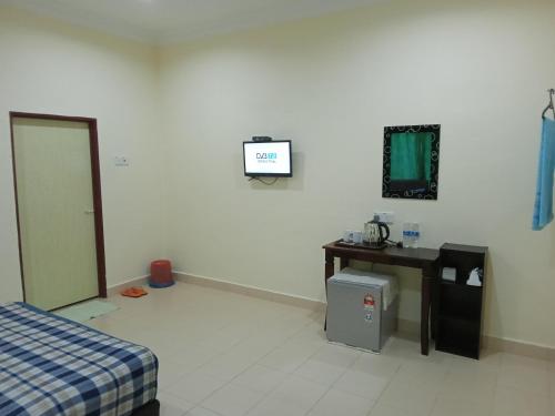 a room with a bed and a desk and a tv at Motel Aurora Damai in Pantai Cenang